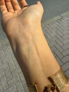 Brown-skinned Wrist with neutral undertone wearing gold jewelry with blue and green vein under natural light